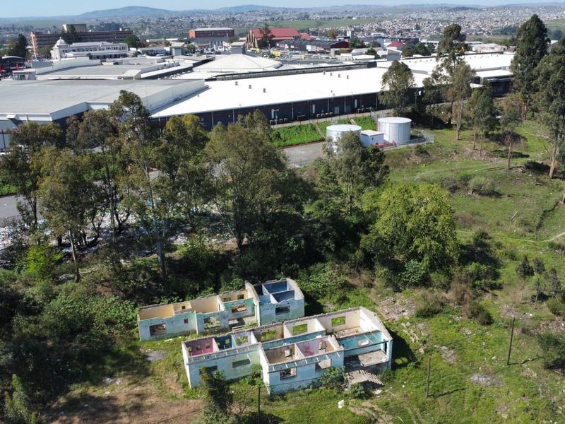 Aerial view of a vacant residential plot featuring a dilapidated, roofless structure in a state of severe disrepair.