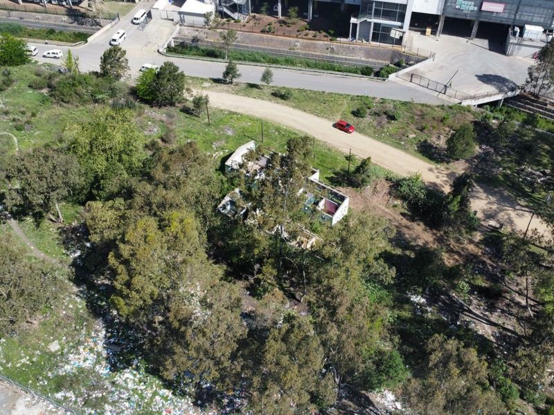 Aerial view of a vacant residential plot featuring mature trees, an unimproved access road, and a dilapidated structure on the property.