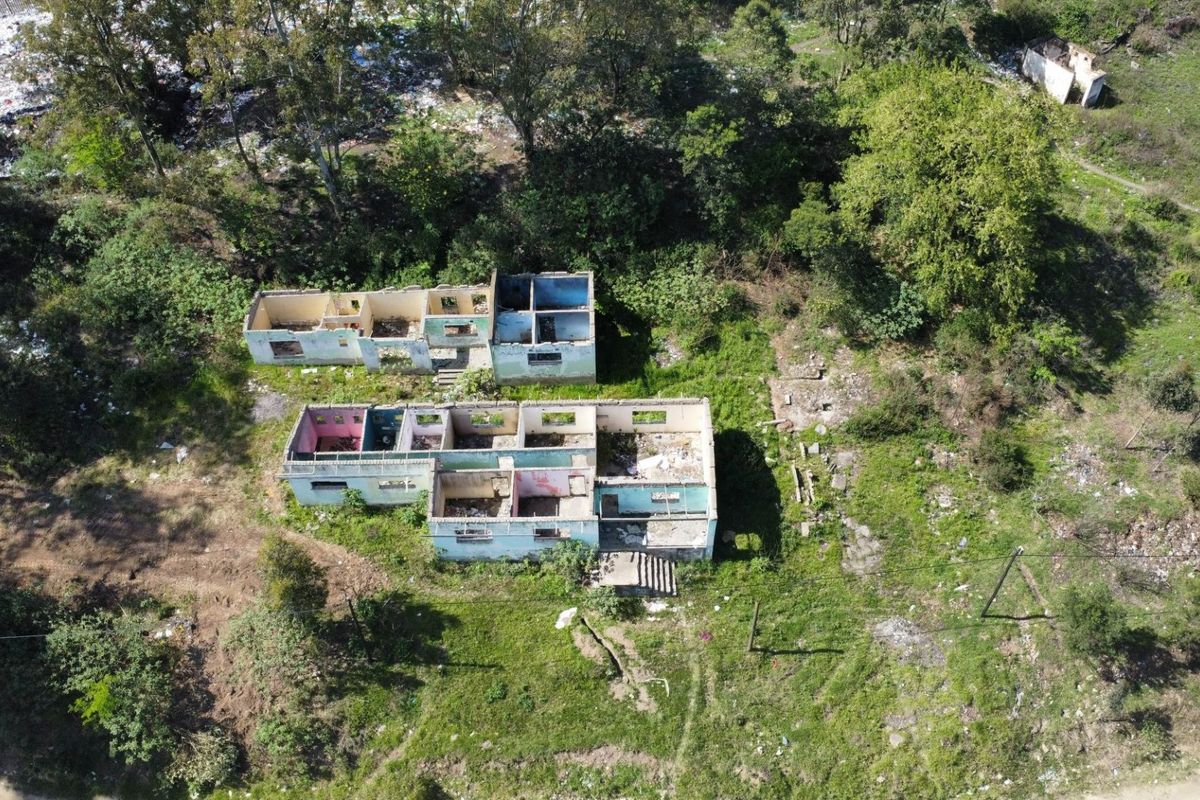 Aerial view of a vacant residential plot featuring the structural shells of two dilapidated buildings requiring significant renovation or demolition.