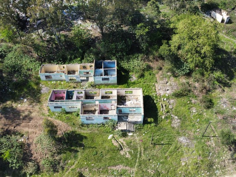 Aerial view of a vacant residential plot featuring the structural shells of two dilapidated buildings requiring significant renovation or demolition.