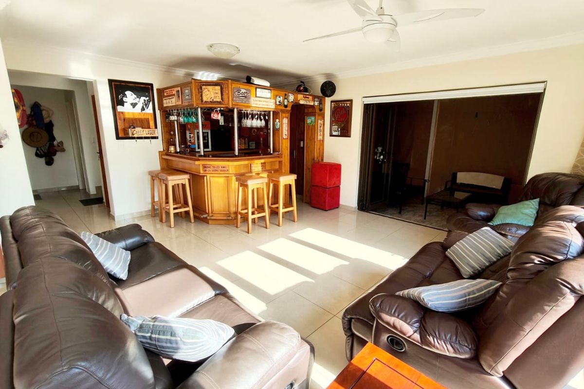 Spacious living area featuring a built-in wooden bar, tiled flooring, ceiling fan, and large sliding doors leading to an outdoor space.