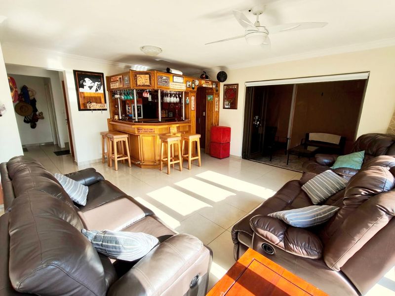 Spacious living area featuring a built-in wooden bar, tiled flooring, ceiling fan, and large sliding doors leading to an outdoor space.