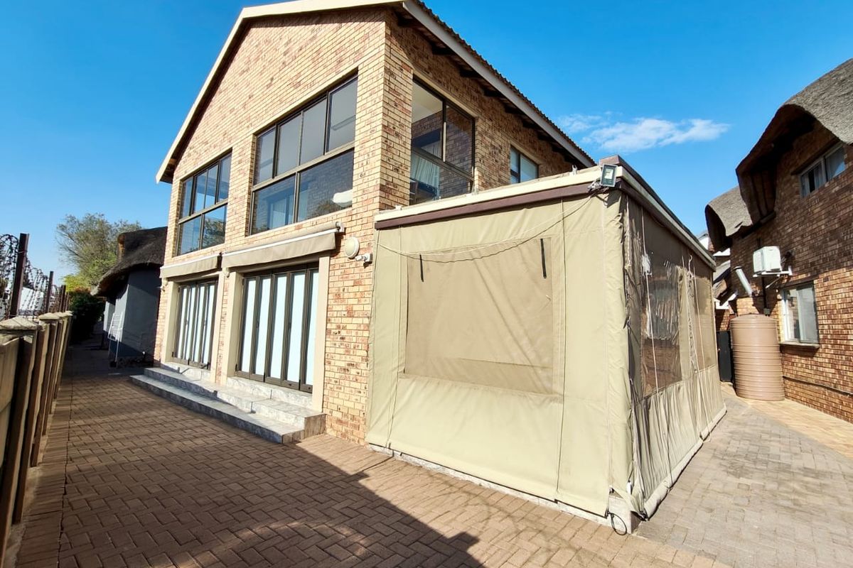 Rear view of a double-story face brick house featuring large windows, sliding doors, and a covered patio area with a canvas enclosure.