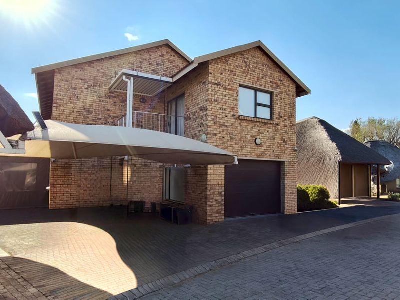 A well-maintained face brick double-story house featuring a paved driveway, integrated single garage, and a shaded carport area.