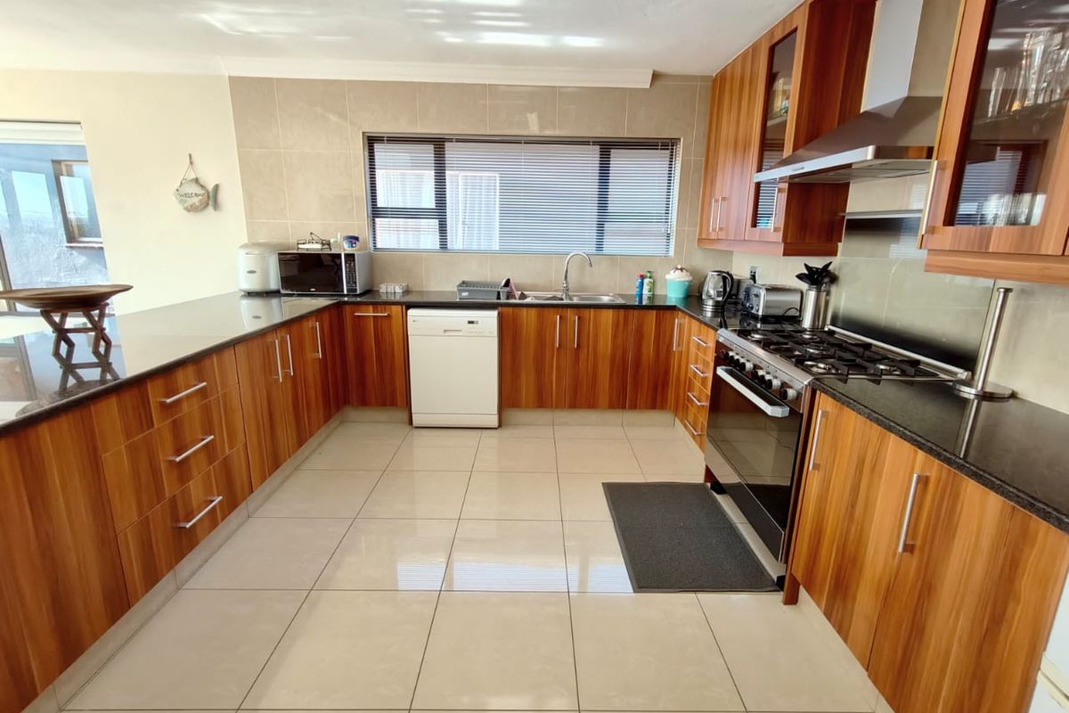 A well-maintained kitchen featuring wood veneer cabinetry, granite countertops, a gas hob with extractor, and tiled flooring throughout.