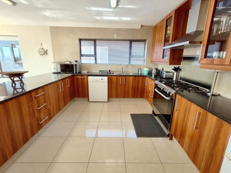 A well-maintained kitchen featuring wood veneer cabinetry, granite countertops, a gas hob with extractor, and tiled flooring throughout.