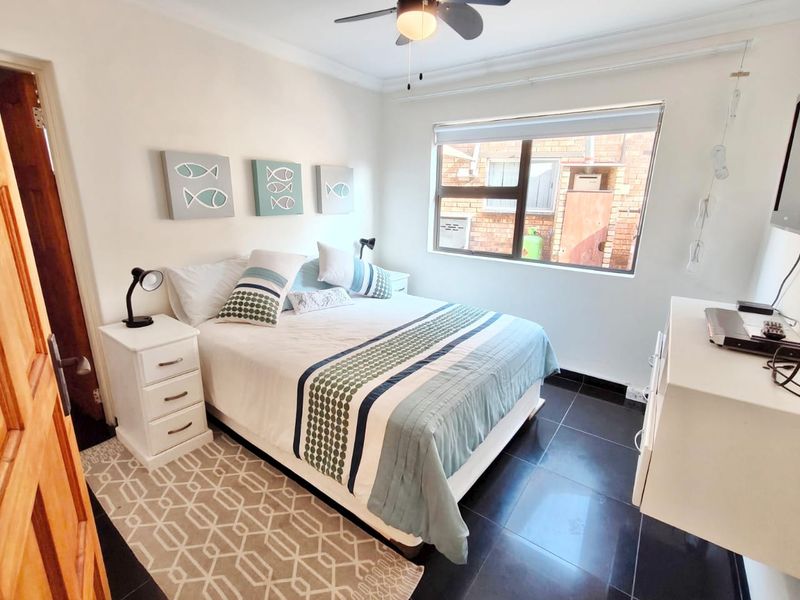 A well-maintained bedroom featuring dark tiled flooring, a ceiling fan, and a large window providing natural light.