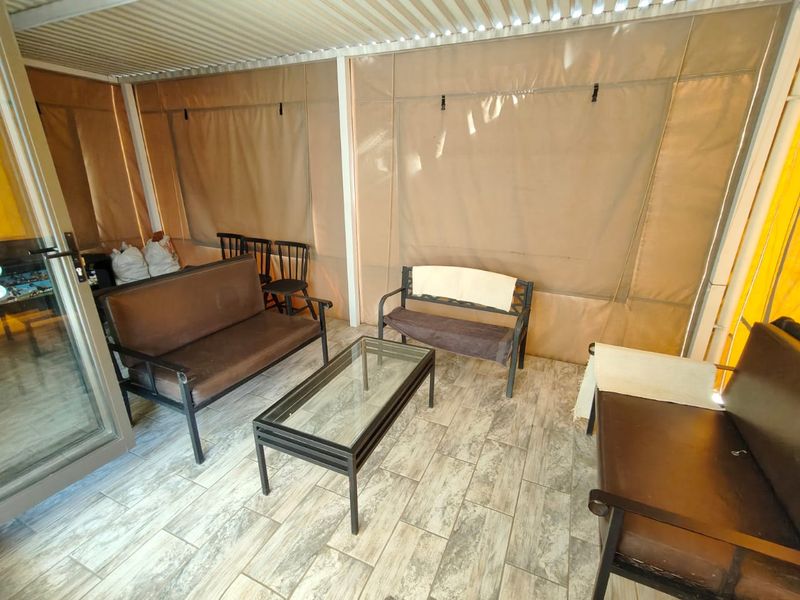 A covered outdoor patio area featuring durable tiled flooring and protective canvas blinds, providing a versatile space for relaxation and entertainment.