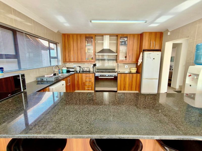 A functional kitchen featuring warm-toned wooden cabinetry, granite countertops, a breakfast bar, and stainless steel appliances, including a gas stove and extractor fan.