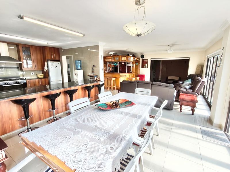 Spacious open-plan living area featuring a modern kitchen with island, dining space, and a built-in bar, finished with tiled flooring and large sliding doors.