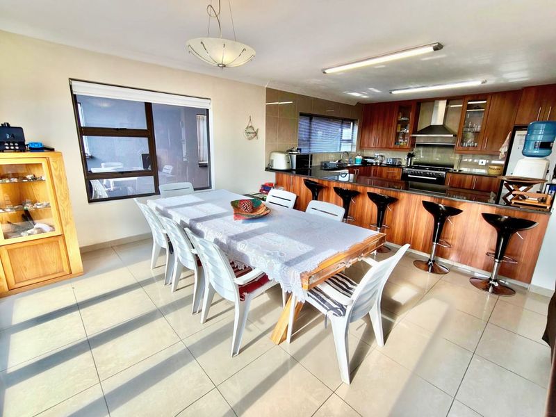 Open-plan kitchen and dining area featuring wood-finish cabinetry, granite countertops, stainless steel extractor fan, and tiled flooring throughout.