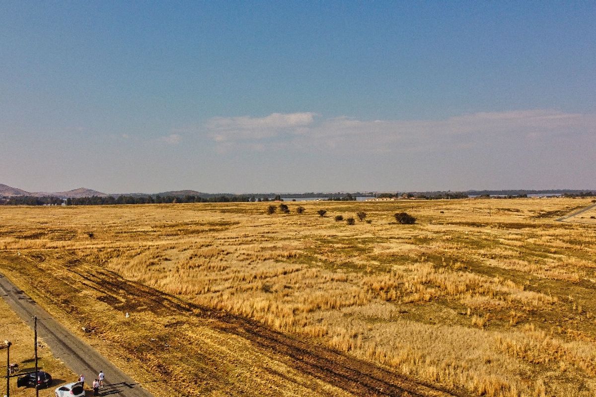 An aerial view of a large, undeveloped residential plot featuring expansive open land and adjacent road access.