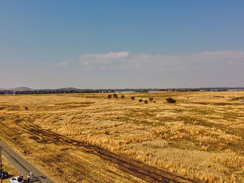 An aerial view of a large, undeveloped residential plot featuring expansive open land and adjacent road access.