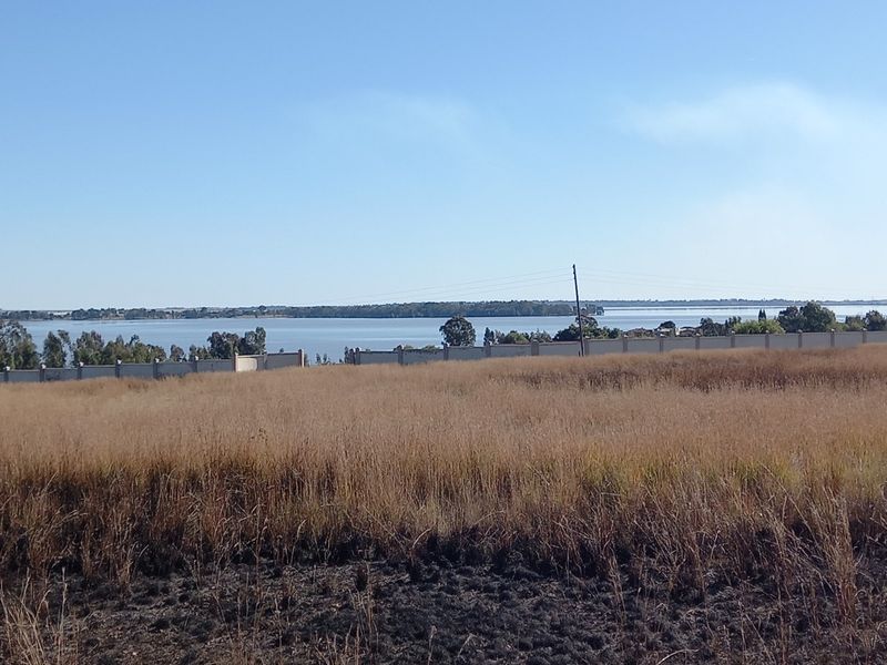 A vacant residential plot featuring expansive views of the nearby lake, enclosed by a perimeter boundary wall.