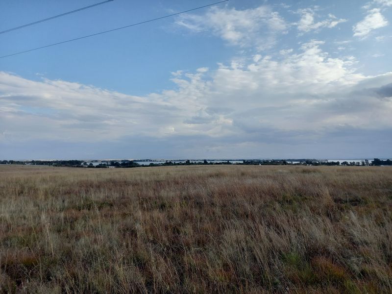 Expansive view of open, undeveloped residential land featuring natural grassland and distant water views under a clear sky.