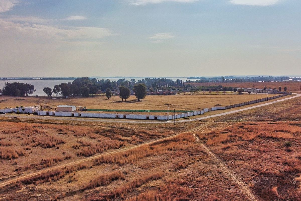 Aerial view of a large vacant residential plot featuring perimeter walling and surrounding landscape with distant water views.