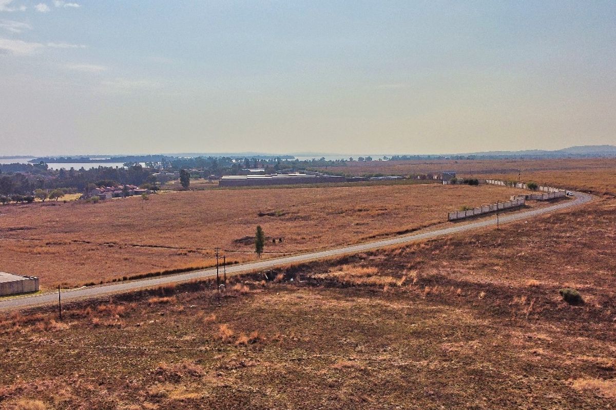 Aerial view of a large vacant residential land parcel featuring road access, boundary walling, and expansive open landscape.