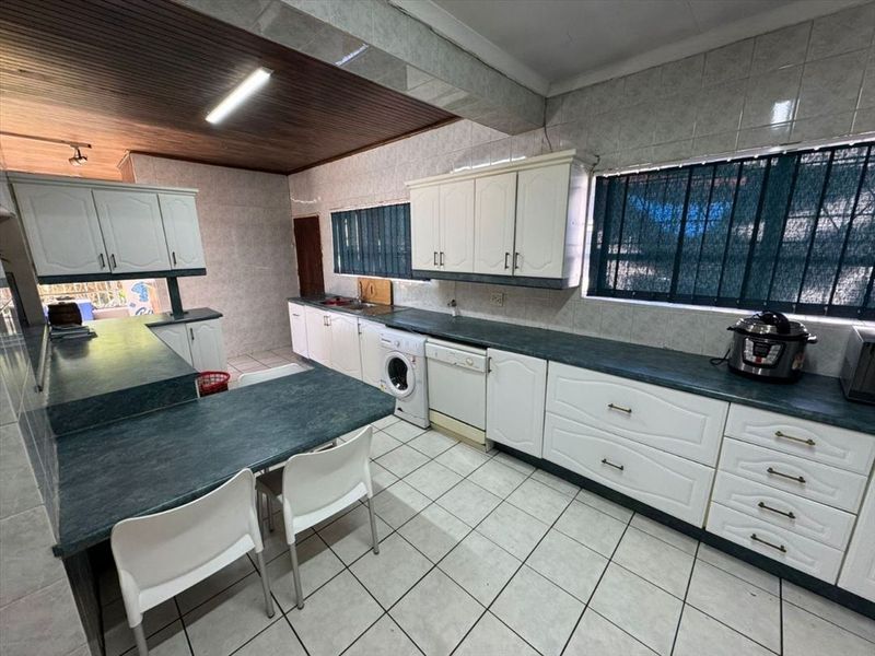 Spacious kitchen featuring extensive built-in cabinetry, laminate countertops, tiled flooring, and integrated laundry appliances under a timber-paneled ceiling.