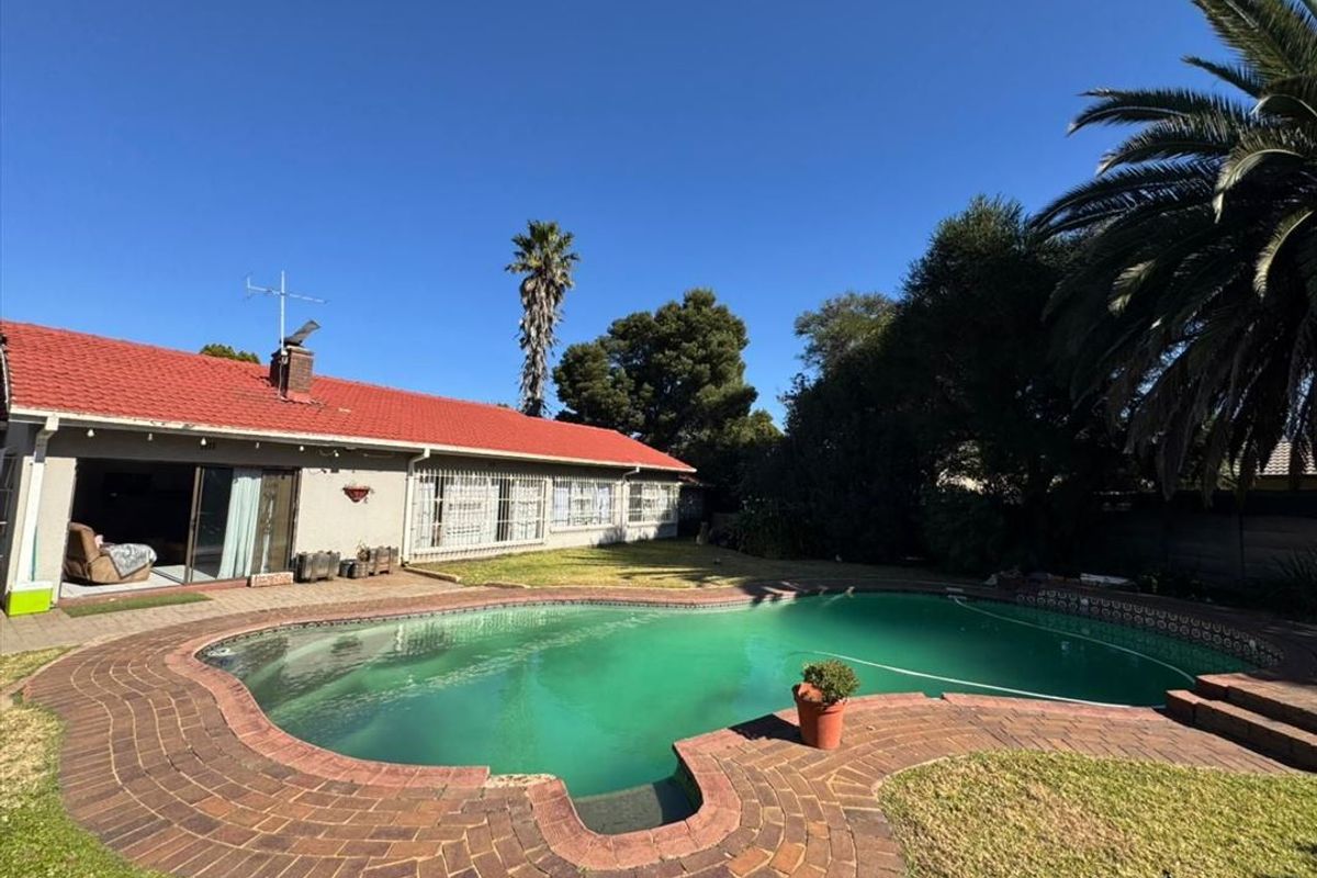 Rear exterior view featuring a swimming pool with brick paving and a house with a red tiled roof.