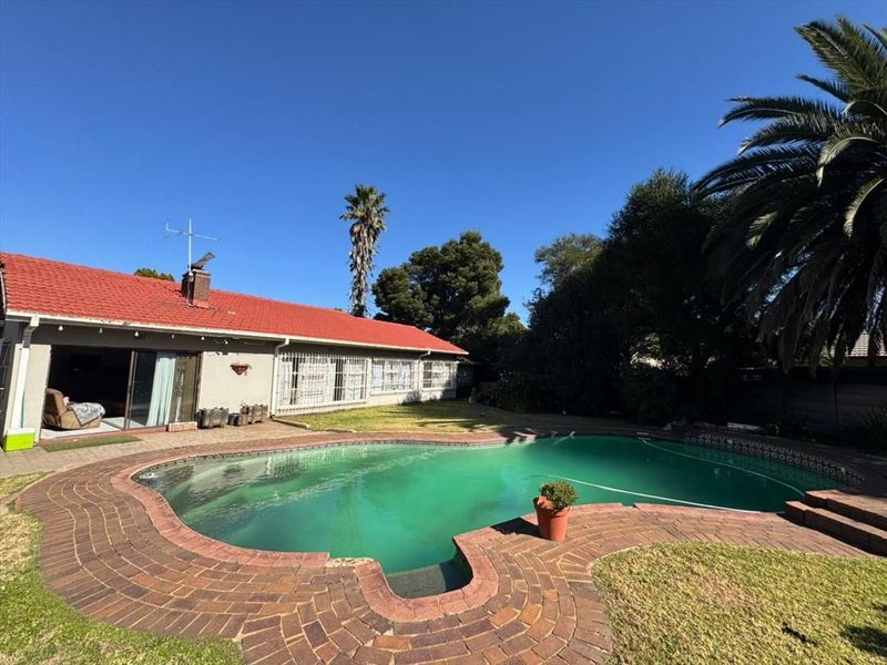 Rear exterior view featuring a swimming pool with brick paving and a house with a red tiled roof.