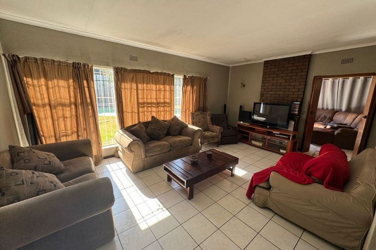 Spacious living room featuring tiled flooring, a brick fireplace, and large windows with security bars, offering potential for a modern update.