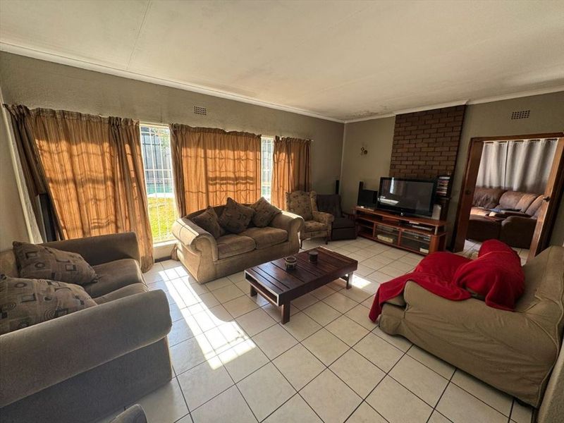 Spacious living room featuring tiled flooring, a brick fireplace, and large windows with security bars, offering potential for a modern update.