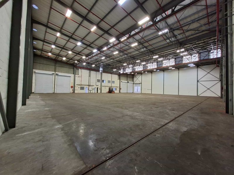 Large, open-plan industrial warehouse space featuring high ceilings, exposed steel structure, roller shutter doors, and durable concrete flooring.
