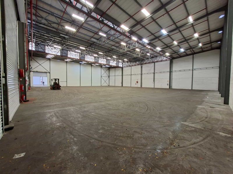 Spacious industrial warehouse featuring a high-clearance steel portal frame, concrete flooring, and large roller shutter access, suitable for logistics or manufacturing operations.