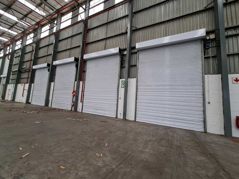 Spacious industrial warehouse interior featuring multiple high-clearance roller shutter doors, exposed steel structural framing, and durable concrete flooring.