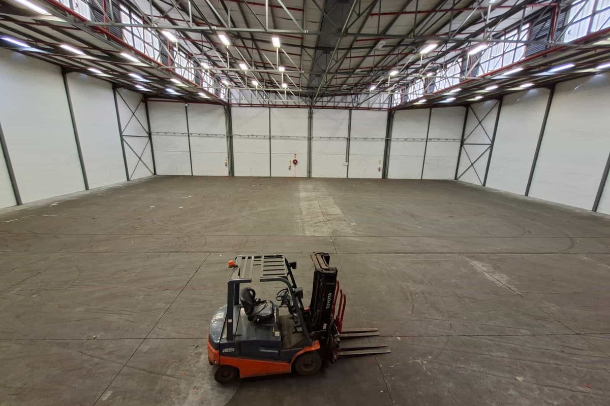 Spacious industrial warehouse unit featuring high ceilings with exposed steel trusses, durable concrete flooring, and overhead fluorescent lighting.