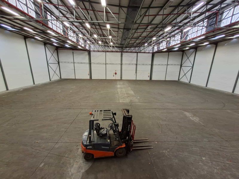 Spacious industrial warehouse unit featuring high ceilings with exposed steel trusses, durable concrete flooring, and overhead fluorescent lighting.