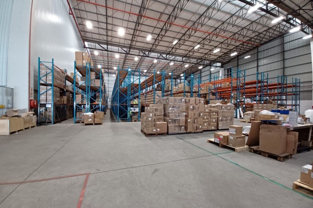 Spacious industrial warehouse featuring high-bay lighting, exposed steel roof trusses, durable concrete flooring, and extensive built-in racking systems for storage.