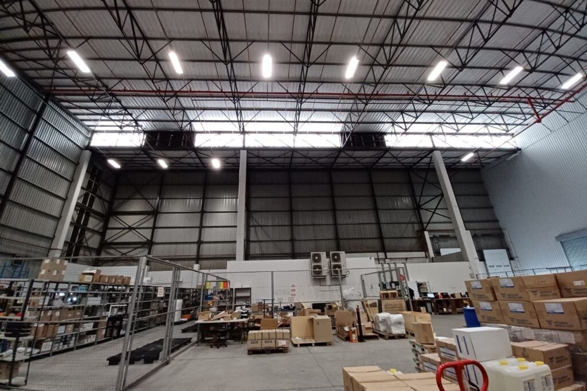 Spacious industrial warehouse featuring high-clearance ceilings, exposed steel trusses, fire sprinkler systems, and durable concrete flooring with wire mesh partitioned storage areas.