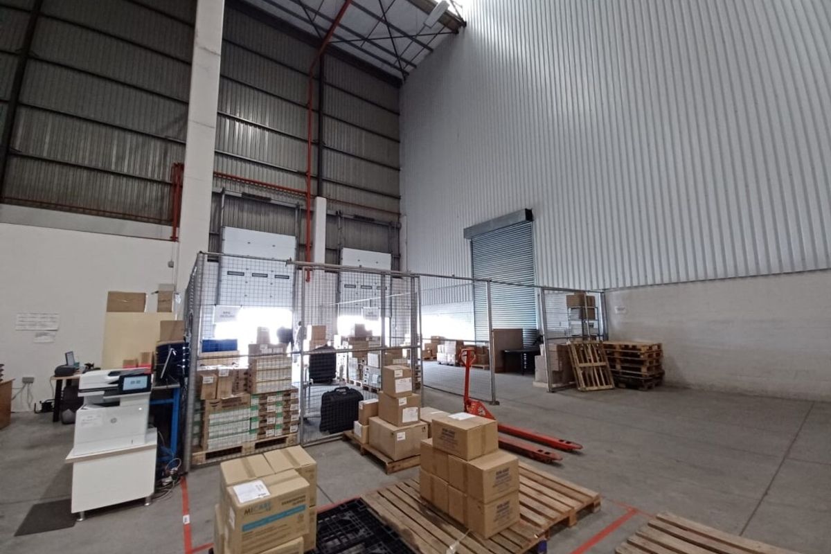 Spacious industrial warehouse area featuring high ceilings, metal cladding, roller shutter doors, and wire mesh partitioning for secure storage and loading operations.