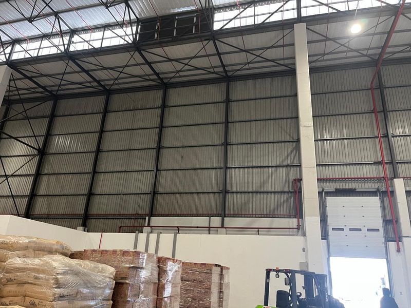 Spacious industrial warehouse interior featuring high ceilings, exposed steel portal frame construction, corrugated metal walls, and a functional roller shutter loading door.