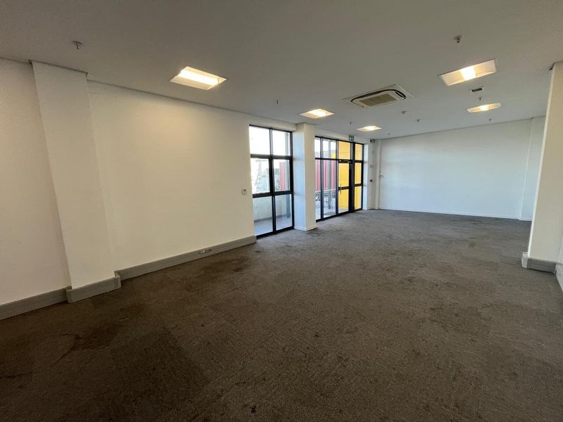 An open-plan office space featuring recessed lighting, ducted air conditioning, and large windows providing natural light.