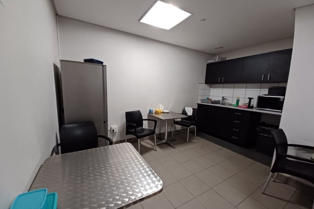 A functional industrial kitchenette featuring dark cabinetry, tiled flooring, and a stainless steel sink, providing a practical break area for staff.