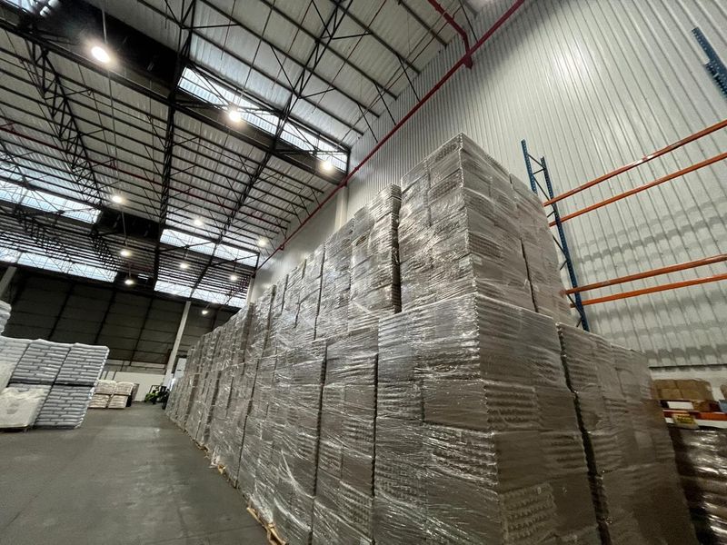 Spacious industrial warehouse featuring high-bay lighting, exposed steel roof trusses, corrugated metal walls, and heavy-duty racking systems for efficient storage.