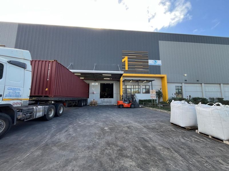 Industrial warehouse exterior featuring a large corrugated metal facade, loading bay access, and a concrete hardstand area suitable for heavy vehicle logistics.
