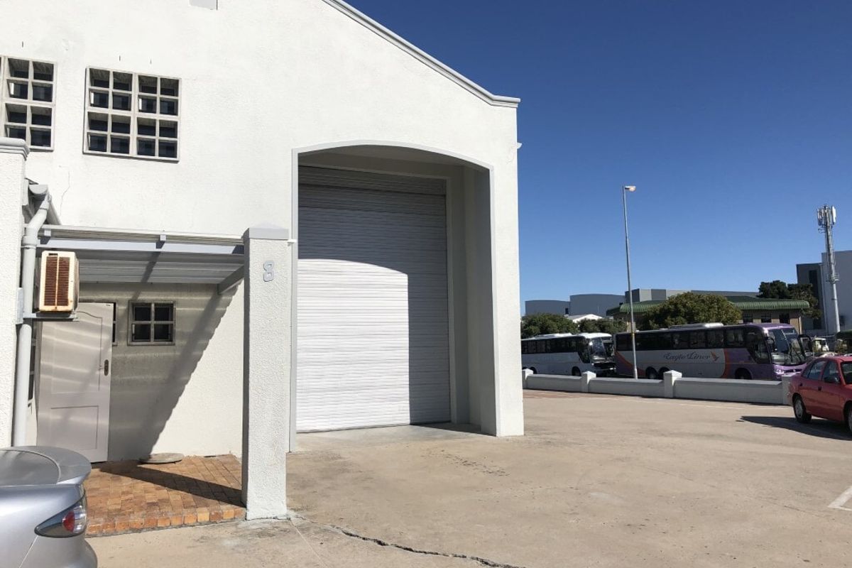 Industrial property exterior featuring a large roller shutter door, concrete driveway, and paved entrance area under a clear blue sky.