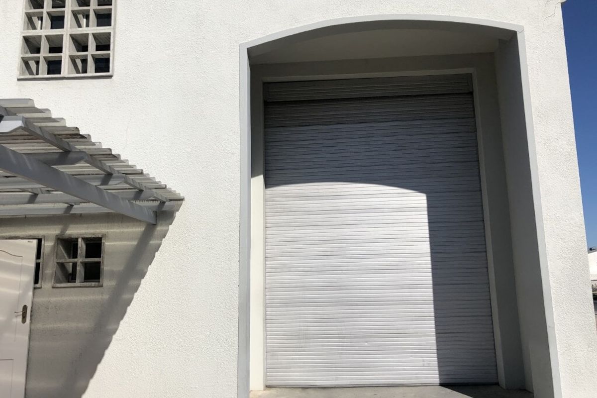 Industrial property exterior featuring a large roller shutter door, concrete facade, and a decorative breeze block window with an attached pergola.