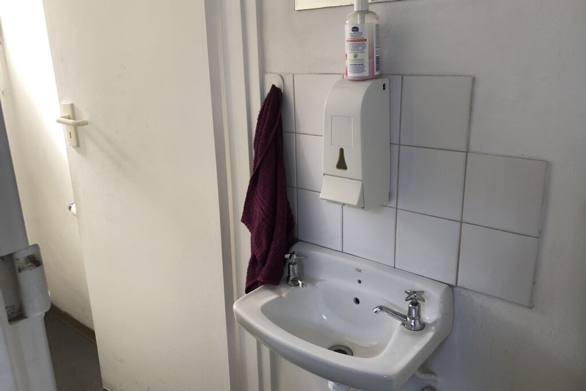 A functional industrial-style washroom featuring a wall-mounted ceramic basin with tiled splashback and a wall-mounted soap dispenser.