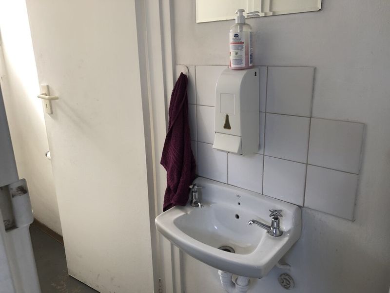 A functional industrial-style washroom featuring a wall-mounted ceramic basin with tiled splashback and a wall-mounted soap dispenser.