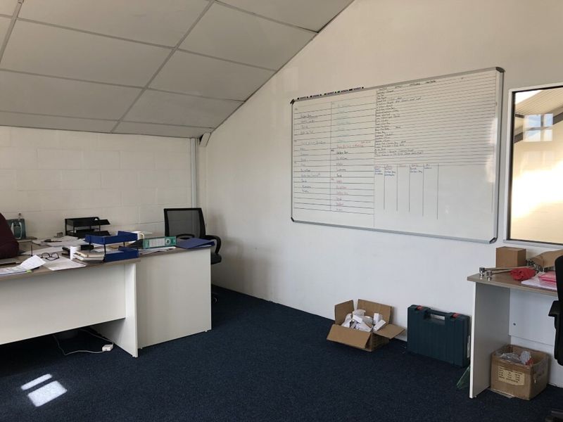 A functional office space featuring a suspended ceiling, carpeted flooring, and a large wall-mounted whiteboard, suitable for administrative or industrial management tasks.