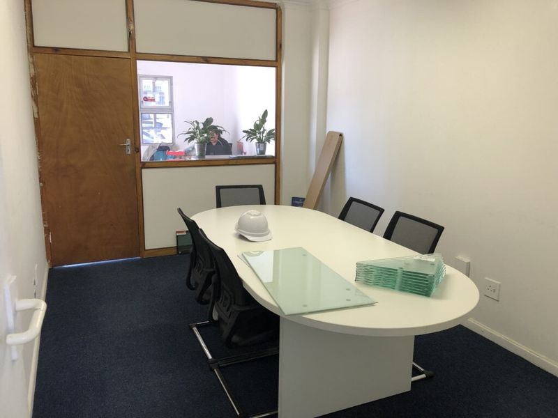 A functional office space featuring blue carpeting, white walls, and an internal glass partition providing visibility into the adjacent area.