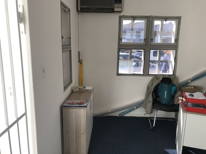 A functional office space featuring carpeted flooring, a wall-mounted air conditioning unit, and security bars on the windows.