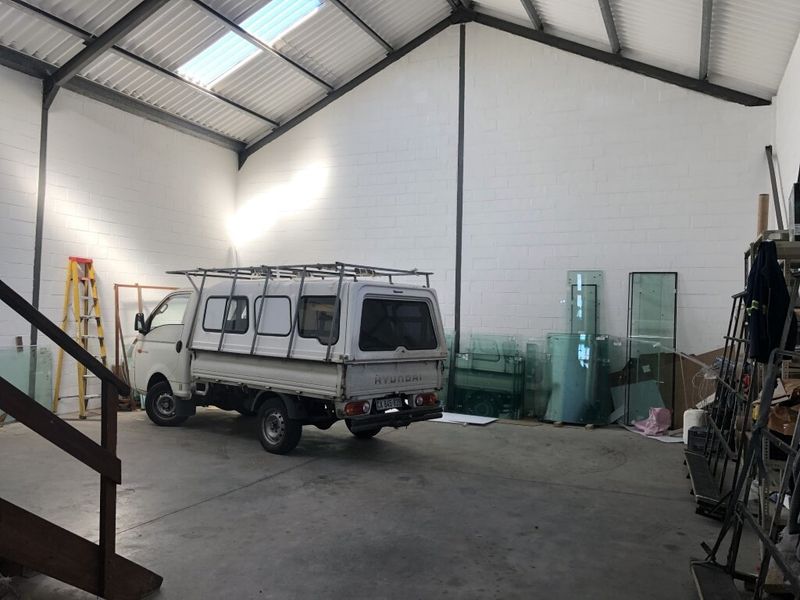 Spacious industrial warehouse or garage area featuring high ceilings with exposed steel trusses, skylights, and durable concrete flooring.