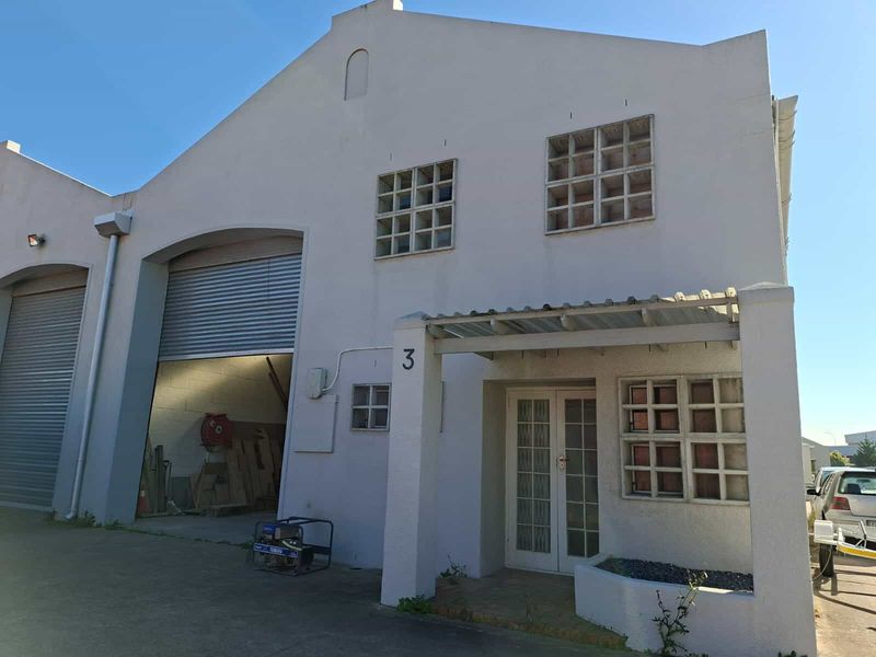 Front elevation of an industrial unit featuring a large roller shutter door, glass block windows, and a covered entrance porch.