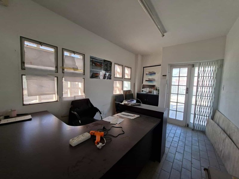 Functional office space featuring tiled flooring, fluorescent lighting, and a secure entrance gate, suitable for administrative or industrial business operations.