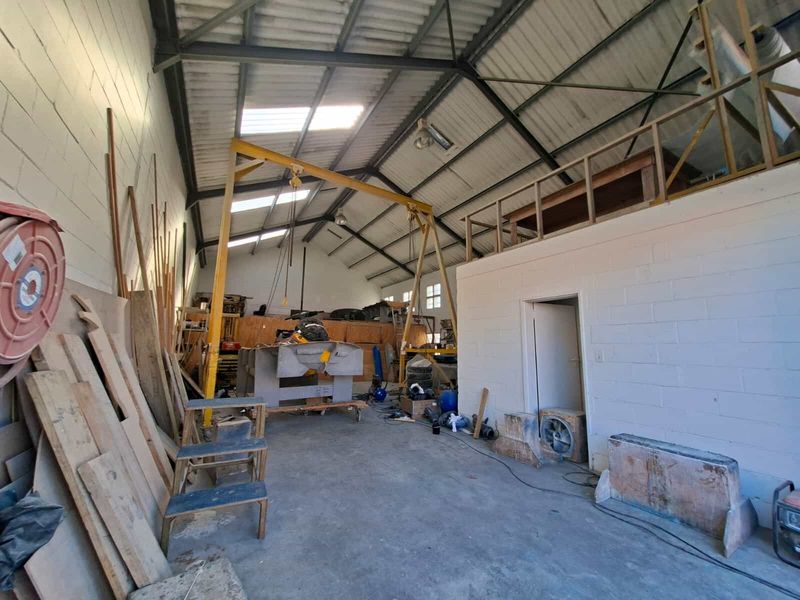 Spacious industrial workshop featuring high ceilings with exposed steel trusses, a mezzanine level, gantry crane, and durable concrete flooring.